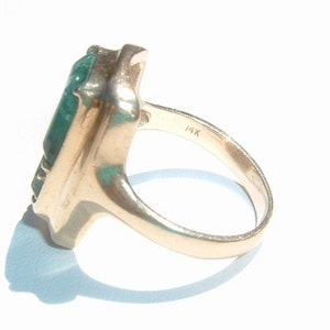 May include: A gold ring featuring a large, rectangular, green gemstone. The ring is marked "14K" on the inside band.