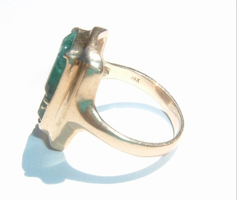 May include: A gold ring featuring a large, rectangular, green gemstone. The ring is marked "14K" on the inside band.