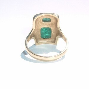 May include: A gold ring with two emerald green gemstones set in a square-shaped design.