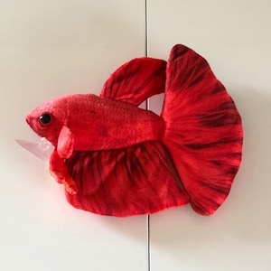Op de afbeelding: Een rood pluche betta-visje speelgoed met zwarte markeringen op zijn vinnen. Het speelgoed is gemaakt van zacht, pluche stof en heeft een realistisch uiterlijk.