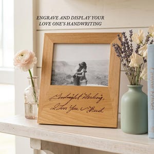 May include: A light-colored wooden picture frame featuring the engraved text "Goodnight Darling, I Love You Bud" on the bottom border. The frame holds a black and white photograph of two people embracing, with the text "ENGRAVE AND DISPLAY YOUR LOVE ONE'S HANDWRITING" visible above the frame.