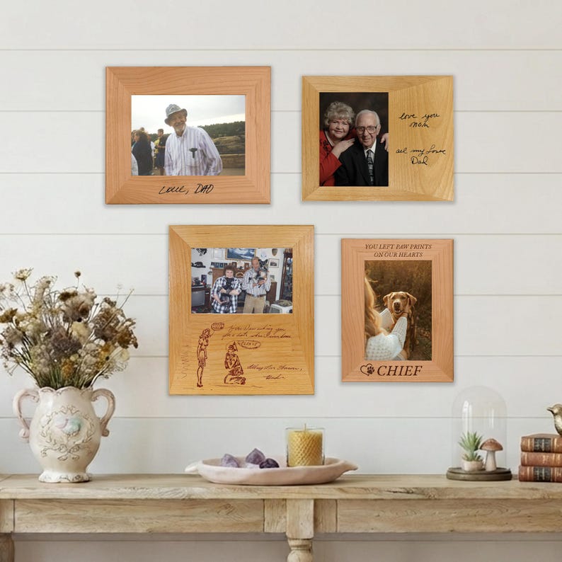 May include: Four light-colored wooden picture frames displayed on a wall. The frames contain various photographs and engraved text, including phrases like Love, Dad, You left paw prints on our hearts, and Chief, along with custom illustrations.