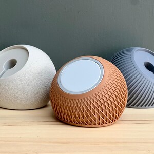 May include: Three spherical charging docks for mobile devices. The left dock is off-white with a textured surface. The center dock is terracotta with a lattice pattern. The right dock is slate blue with vertical ridges. Each features a circular center.