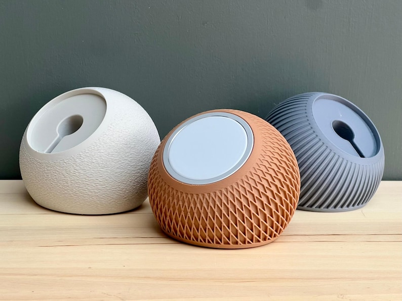 May include: Three spherical charging docks for mobile devices. The left dock is off-white with a textured surface. The center dock is terracotta with a lattice pattern. The right dock is slate blue with vertical ridges. Each features a circular center.