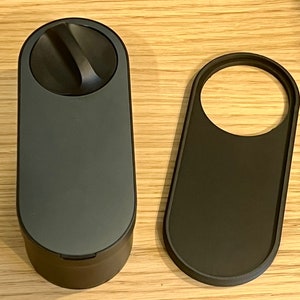 May include: A black cylindrical container with a round lid and a small handle on the lid. The container is next to a black oval-shaped object with a circular cutout.
