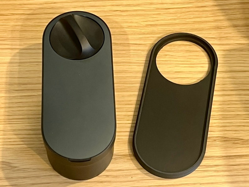May include: A black cylindrical container with a round lid and a small handle on the lid. The container is next to a black oval-shaped object with a circular cutout.