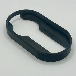 May include: A black, 3D-printed bottle opener with an oval shape and a keyhole-like opening. The opener is made of a solid, matte black material and is designed for easy grip and leverage.