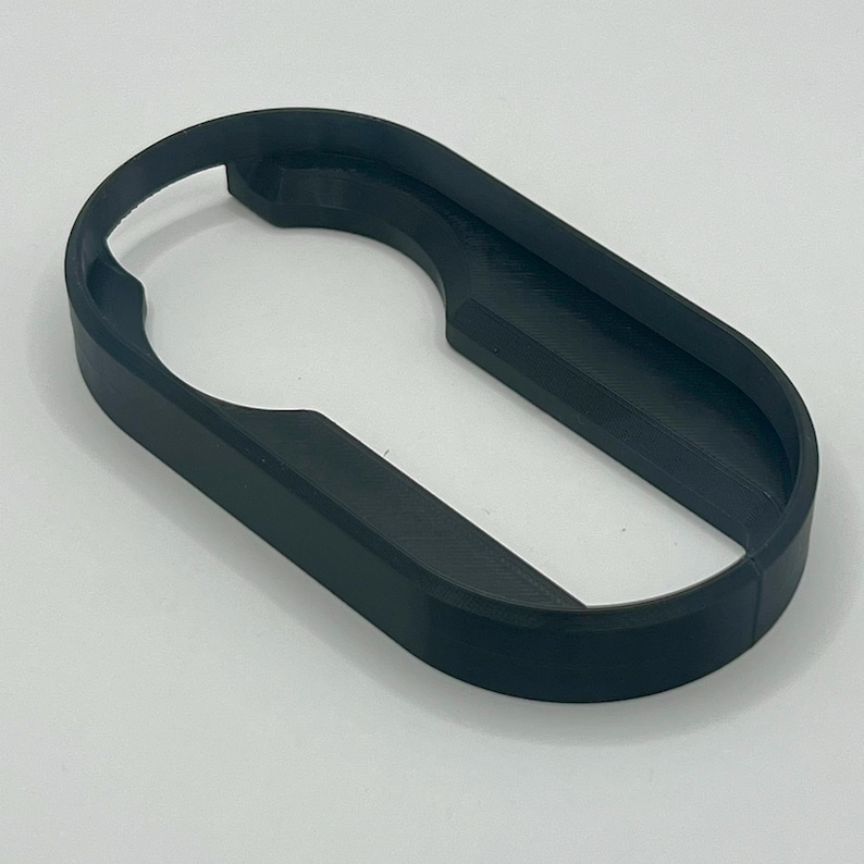 May include: A black, 3D-printed bottle opener with an oval shape and a keyhole-like opening. The opener is made of a solid, matte black material and is designed for easy grip and leverage.