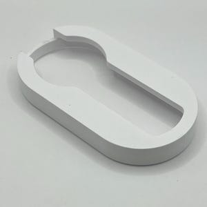 May include: A white, oval-shaped object with a keyhole-like cutout. The object has a smooth, matte finish and a rounded, raised edge. The design is simple and modern, with a clean aesthetic. The object appears to be a decorative or functional item.