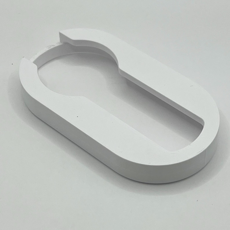 May include: A white, oval-shaped object with a keyhole-like cutout. The object has a smooth, matte finish and a rounded, raised edge. The design is simple and modern, with a clean aesthetic. The object appears to be a decorative or functional item.