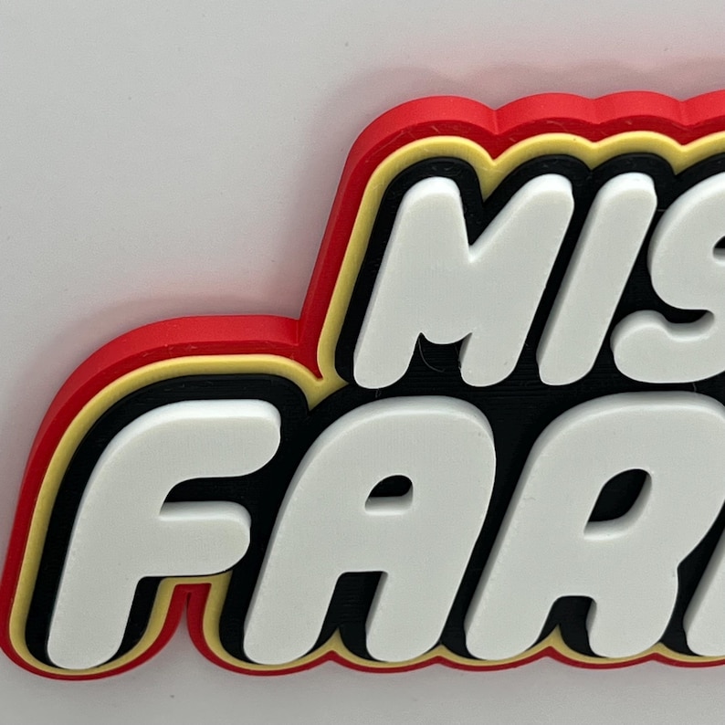 May include: A 3D printed sign with the words "Misfit" and "Far" in white letters with black outlines and a red and gold border.
