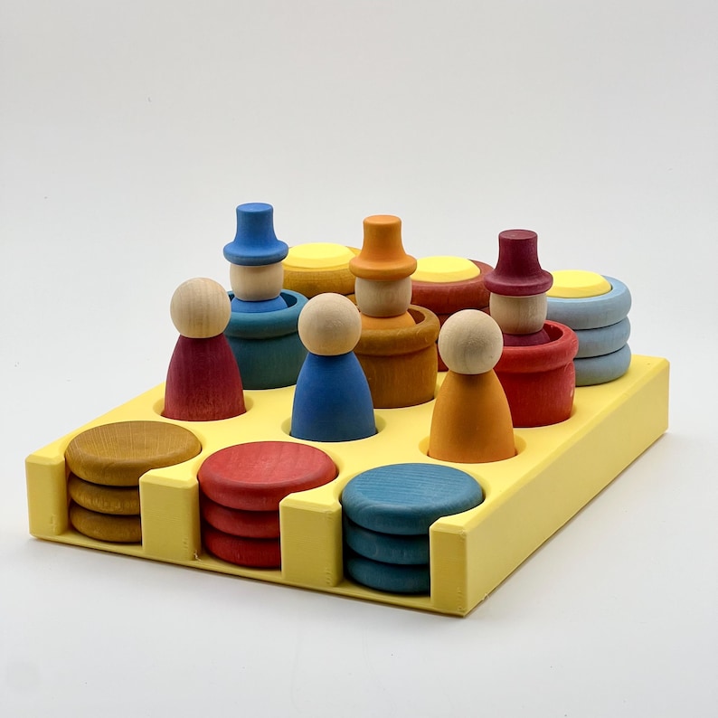 May include: A yellow wooden tray with nine circular compartments holds colorful wooden stacking toys. The toys include small people with hats and round discs in various colors.