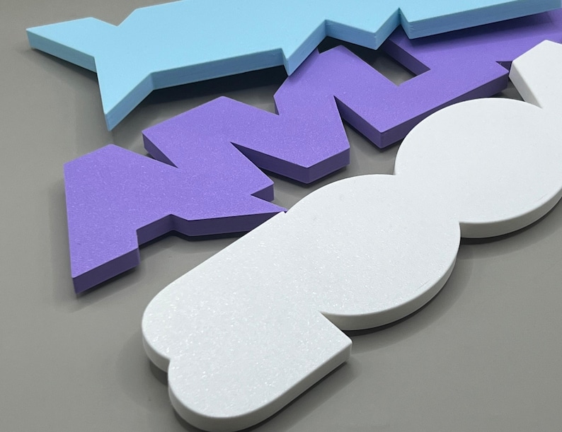 May include: Close-up of colorful foam shapes in light blue, purple, and white. The shapes are geometric and appear to be part of a larger design or puzzle. The foam has a textured surface, and the background is a solid gray.