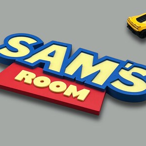 May include: A colorful sign that reads "SAM'S ROOM" in yellow and blue letters on a red background. A yellow toy car is in the upper right corner. The sign is likely for a child's bedroom.