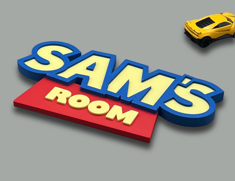 May include: A colorful sign that reads "SAM'S ROOM" in yellow and blue letters on a red background. A yellow toy car is in the upper right corner. The sign is likely for a child's bedroom.