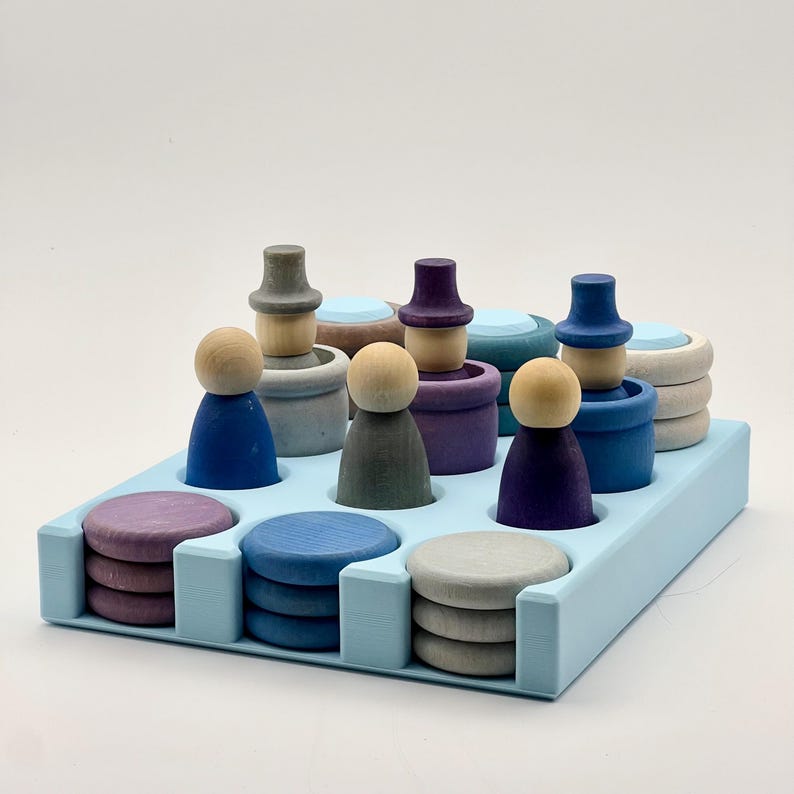 May include: A blue wooden tray with nine wooden figures and three stacks of wooden circles. The figures are painted in shades of blue, purple, and gray. The circles are painted in shades of blue, purple, and gray.