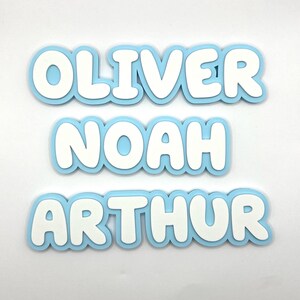 May include: Three blue and white foam letters spelling out the names "Oliver", "Noah", and "Arthur".