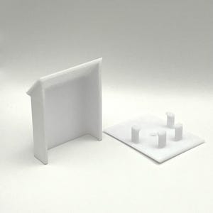May include: Two white plastic pieces, one a rectangular base with four small raised circles, the other a rectangular box with an open front.