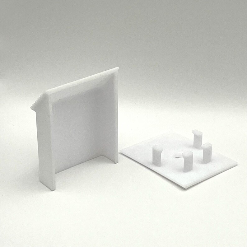 May include: Two white plastic pieces, one a rectangular base with four small raised circles, the other a rectangular box with an open front.