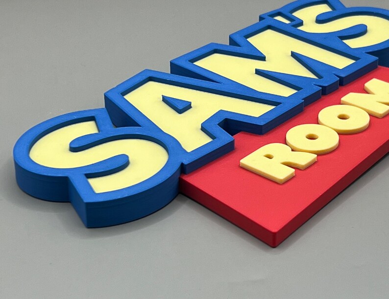 May include: A colorful sign that reads "SAM'S ROOM." The letters are yellow with blue outlines, set against a red background. The sign is designed with a 3D effect, creating a playful and eye-catching appearance.