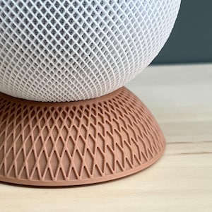 May include: A spherical object with a white lattice structure resting on a circular base with a peach-coloured diamond grid pattern. The top section features a dense, interconnected white mesh design, while the bottom section is a solid peach-coloured base.
