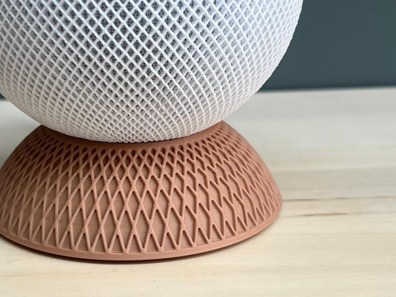 May include: A spherical object with a white lattice structure resting on a circular base with a peach-coloured diamond grid pattern. The top section features a dense, interconnected white mesh design, while the bottom section is a solid peach-coloured base.
