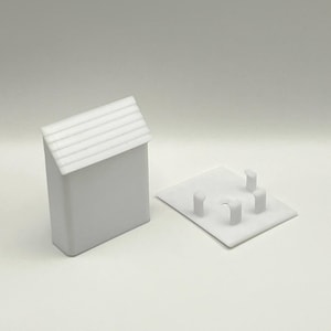 May include: White plastic model of a small building with a gabled roof and a base with four small pillars. The model is designed to be used as a miniature building for a model train set.