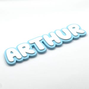 May include: A light blue and white 3D name sign that reads "ARTHUR".
