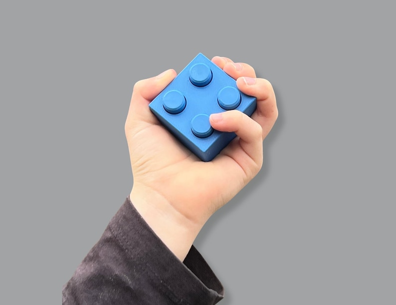 May include: A bright blue building block with four circular studs on top. The block is held in a hand against a gray background. The block is a solid, vibrant color.
