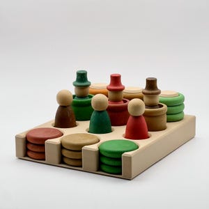 May include: A wooden toy set with colorful stacking figures and circles. The figures have different colored hats and bodies. The circles are stacked in different colors and sizes. The set is arranged on a wooden tray.