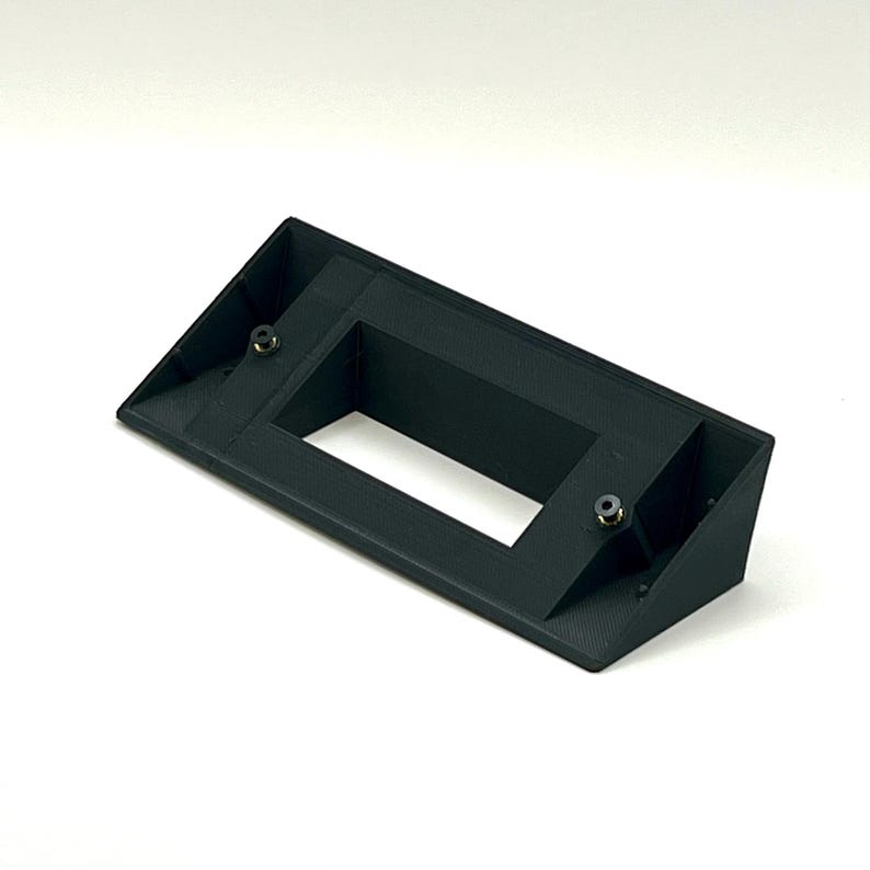 May include: Black plastic wall mount with a rectangular opening. The mount has two small screws on the sides.