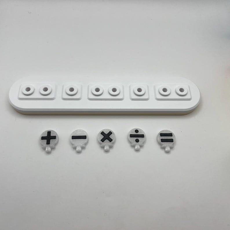 May include: A white plastic tray with six round holes and five white plastic buttons with black mathematical symbols: plus, minus, multiply, divide, and equals.