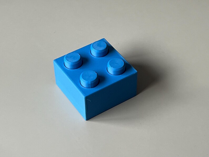 May include: A bright blue building block with four raised studs on top. The block is square and has a smooth, solid appearance. The image is taken from a slightly elevated angle, showcasing the block's form.