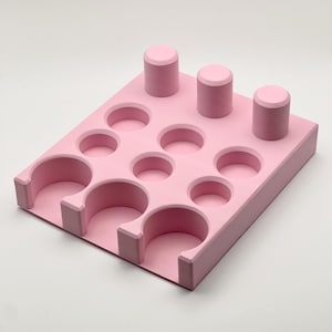 May include: Pink plastic organizer with 12 round compartments and 3 vertical slots. The organizer is designed to hold small items like nail polish or essential oils.