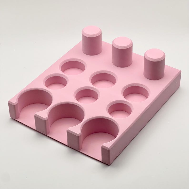 May include: Pink plastic organizer with 12 round compartments and 3 vertical slots. The organizer is designed to hold small items like nail polish or essential oils.