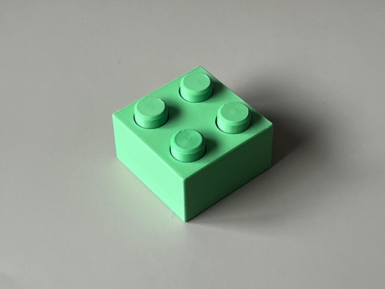 May include: A solid green building block with four raised circular studs on top. The block is square-shaped and has a smooth, matte finish. The color is a vibrant, light green.