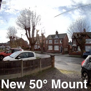 May include: A wide-angle view of a residential street with houses and trees. A black car is parked in the driveway, and a white car is parked in the street. The text "New 50&deg; Mount" is visible in the lower right corner of the image.