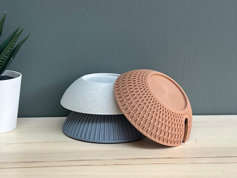 May include: Three stacked bowls in different colours and textures. The top bowl is white with a wavy surface, the middle bowl is dark grey with vertical ridges, and the front bowl is terracotta with a geometric diamond-shaped lattice pattern.