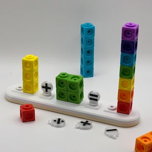 May include: A colourful set of counting blocks with a white base and black maths symbols. The blocks are stacked in columns and include a yellow, green, blue, and rainbow stack. The symbols include plus, minus, equals, and divide.