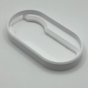 May include: A light gray, oval-shaped tray with a white interior. The tray has a curved section on one side and a raised edge. The design is minimalist and modern, suitable for organizing small items.