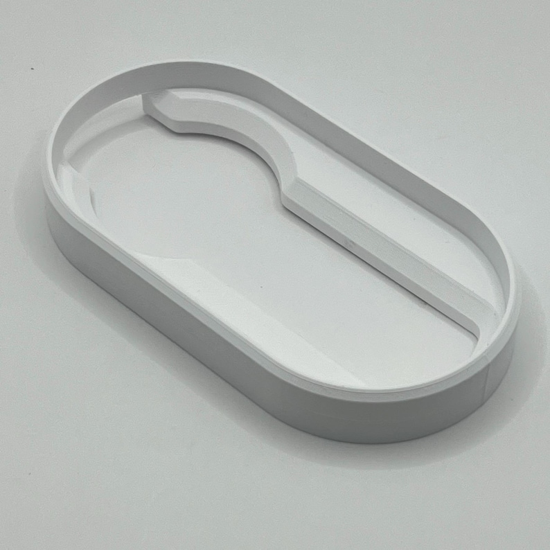 May include: A light gray, oval-shaped tray with a white interior. The tray has a curved section on one side and a raised edge. The design is minimalist and modern, suitable for organizing small items.