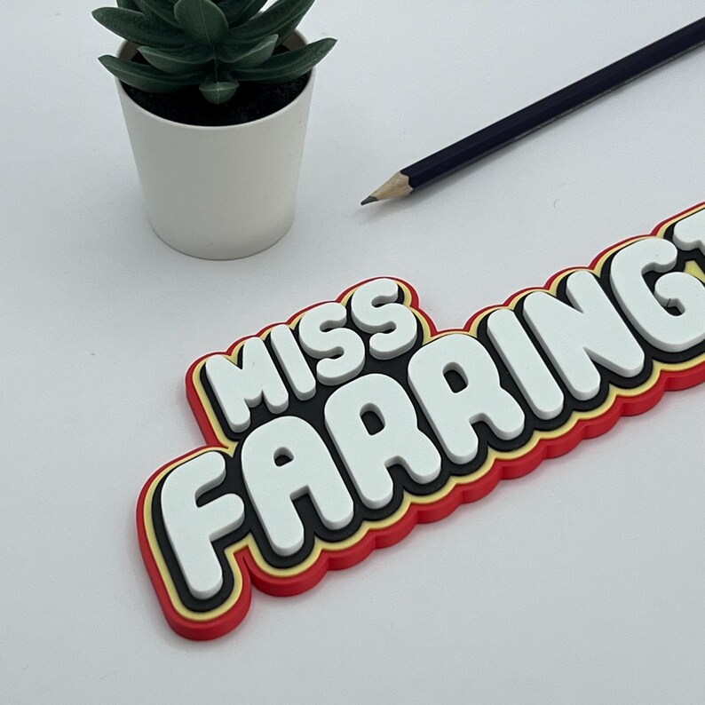 May include: A red, yellow, and black 3D plastic sign that says "Miss Farring" in white letters.