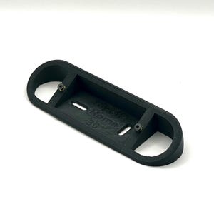 May include: Black plastic 3D printed part with two holes and the text "WARNING HOT SURFACE 30C" printed on the surface.