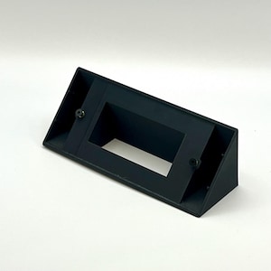 May include: A black plastic wall mount with a rectangular opening. The mount has two screw holes on the side.