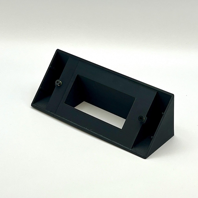 May include: A black plastic wall mount with a rectangular opening. The mount has two screw holes on the side.