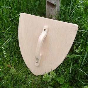 May include: A light-colored wooden shield with a smooth, unfinished surface and a curved, pointed bottom edge. A matching wooden handle is securely attached to the center of the shield, featuring two visible screw holes for mounting purposes.