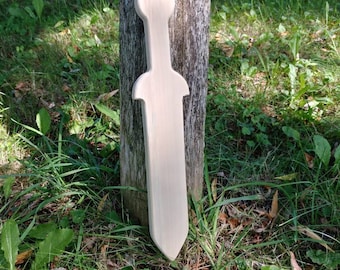 May include: A wooden toy sword with a rounded tip, painted white, leaning against a wooden post. The sword is in a grassy area.