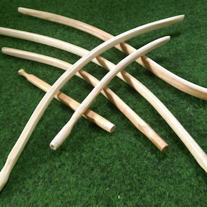 Könnte beinhalten: Sechs Holzstäbe, alle in eine gebogene Form gebogen. Die Stäbe sind in einem Kreuzmuster auf einer grünen Oberfläche angeordnet.