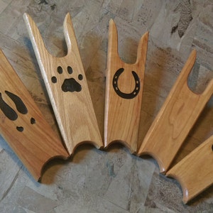 May include: Six wooden boot jacks with different designs. The designs include a horseshoe, a paw print, and a deer track. The boot jacks are all made of light brown wood.
