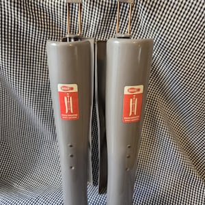 May include: A pair of grey plastic Dascomatic boot shapers featuring a vertical design with a top hanging hook and a red rectangular label on the front of each unit. The label displays the Dasco logo and the text Dascomatic Boot Shaper.